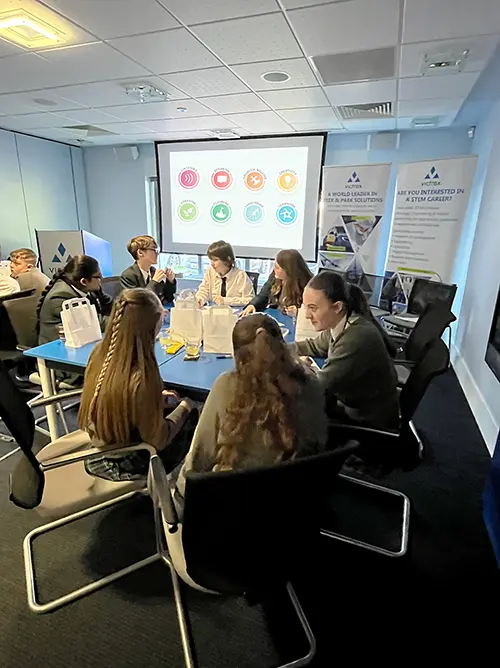 A group of teenage schoolchildren sat at a desk taking part in a Skills Builder activity facilitated by an employer.