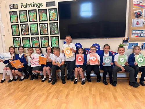 A group of primary school pupils sat in a line smile with glee as they hold up posters of the skills icons.