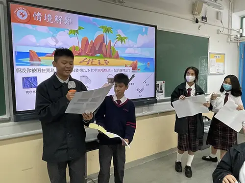 Two students in Hong Kong stand up and deliver a presentation together whilst reading from a crib sheet that they prepared for themselves.
