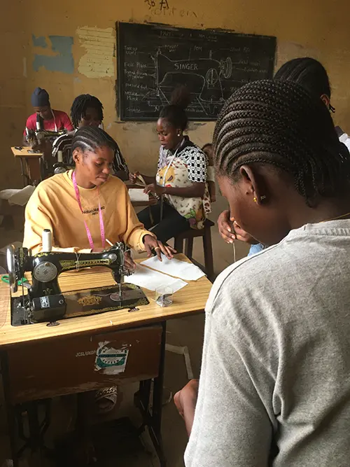 A group of women refugees in Nigeria learn essential skills whilst in a textiles class with sewing machines.
