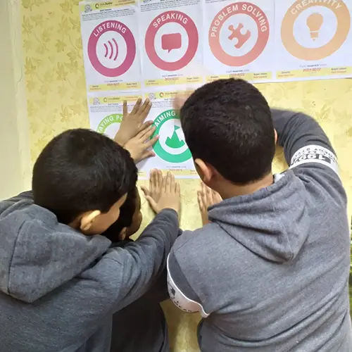 To Lebanese boys stick Skills Builder posters up onto the wall of their classroom.