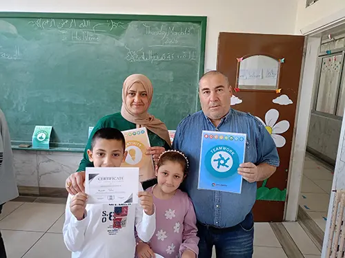Two Lebanese school kids stand proudly in front of their mother and father, who is holding up a skills award for Leadership. 