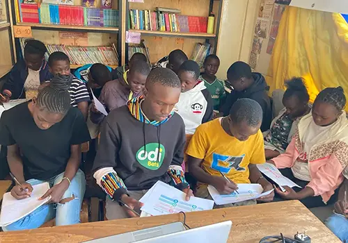 A group of older students in Kenya sit together and revise in a classroom.