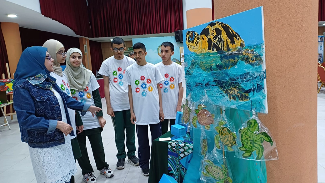 An image showing a teacher giving instructions to a group of older students, aged 16-71. These students are Skills Mentors, they help other students in the school with recognising and building their essential skills. They are wearing white t-shirts with the eight essential skills icons on them.