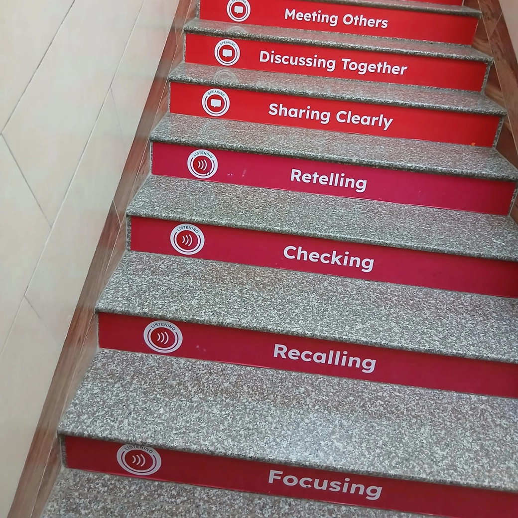 A set of stairs with the Universal Framework steps pasted onto the outer edge of each stair. The steps visible is Focusing, Recalling, Checking, Retelling, Sharing Clearly, Discussing Together and Meeting Others.