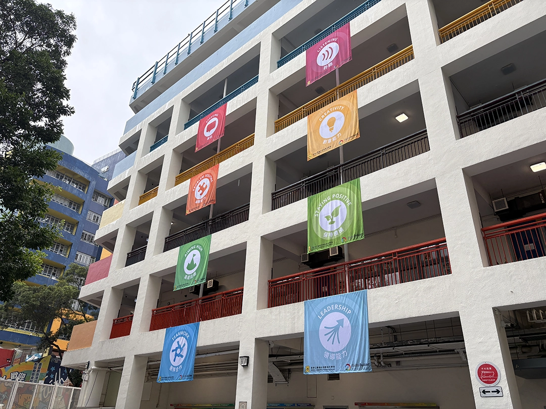 An image of the outside of a school building in Honk Kong. Over the balcony on each floor, is a large banner - each with an essential skill icon.