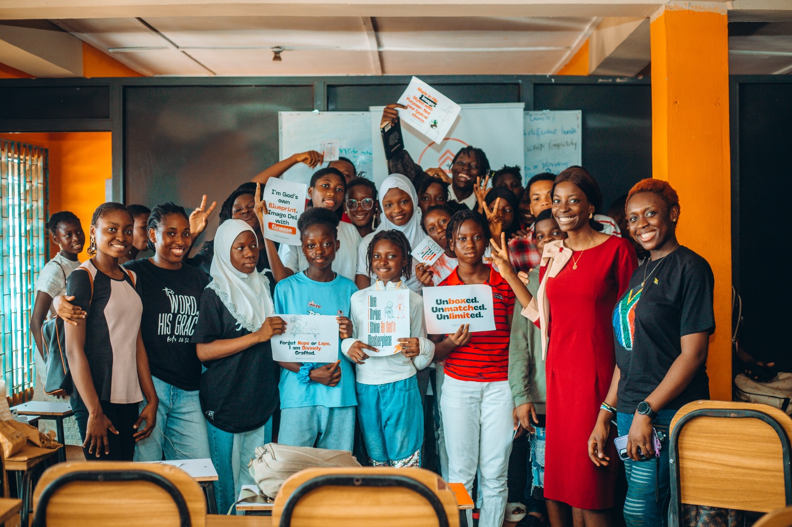 A group of smiling students and teachers holding inspirational printed signs in a classroom