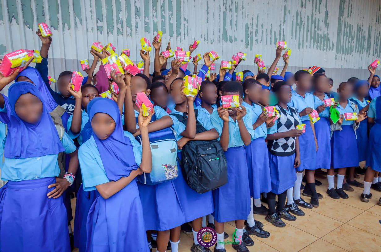 Schoolgirls in blue uniforms hold up packages of sanitary pads