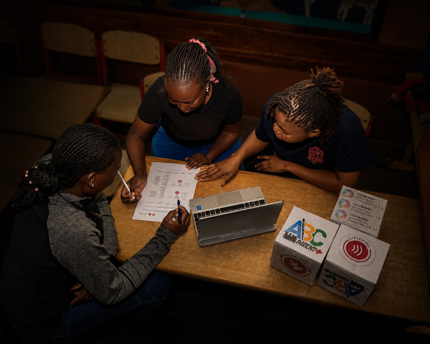 Three women collaborate around a laptop, ABC Parent Plus kit and Skills Builder resources