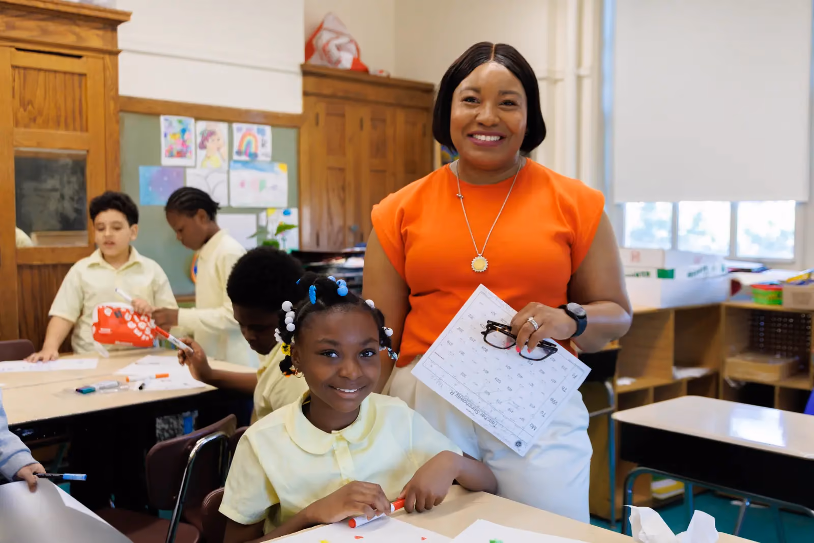 Teacher smiling with young student at classroom desk