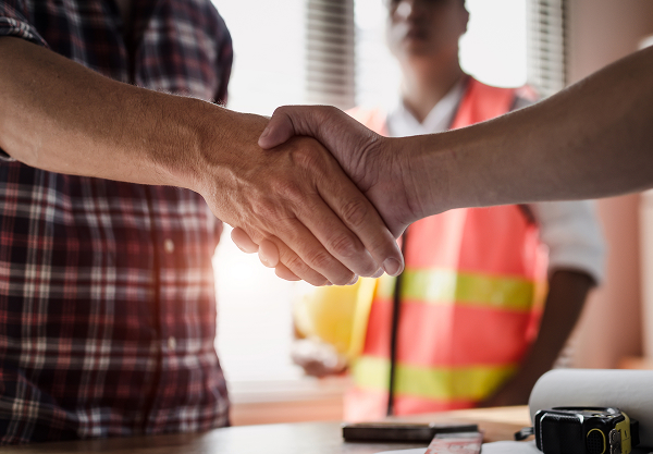 Deux personnes se serrant la main, l'une portant une chemise à carreaux et l'autre un gilet de sécurité orange avec des bandes réfléchissantes, en arrière-plan.