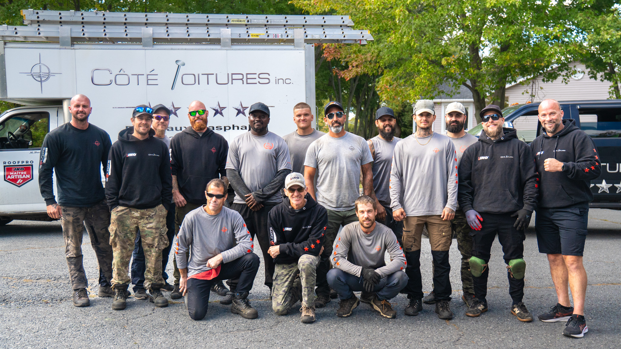 Groupe de quinze hommes portant des vêtements de travail posant devant deux camionnettes de l'entreprise Côté Toitures inc.