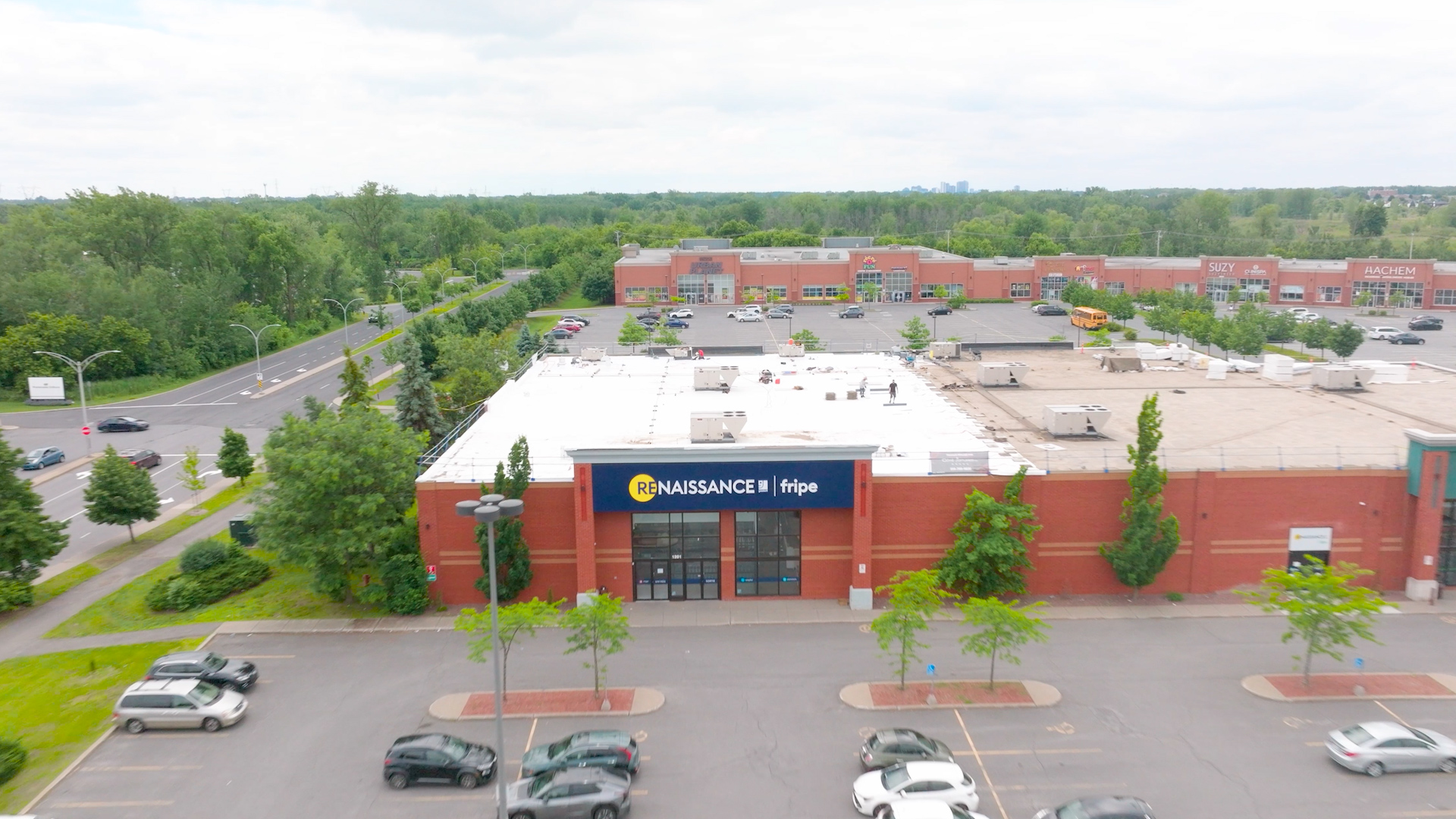 Vue aérienne d'un centre commercial avec un grand magasin Renaissance fripes en brique rouge et un parking avec quelques voitures garées.