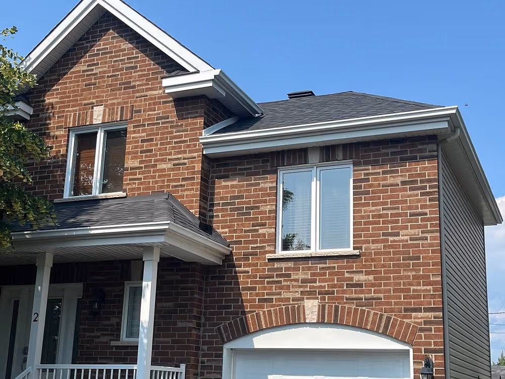 Maison en brique rouge avec un porche couvert, une porte d'entrée blanche et des fenêtres blanches sous un ciel bleu clair.