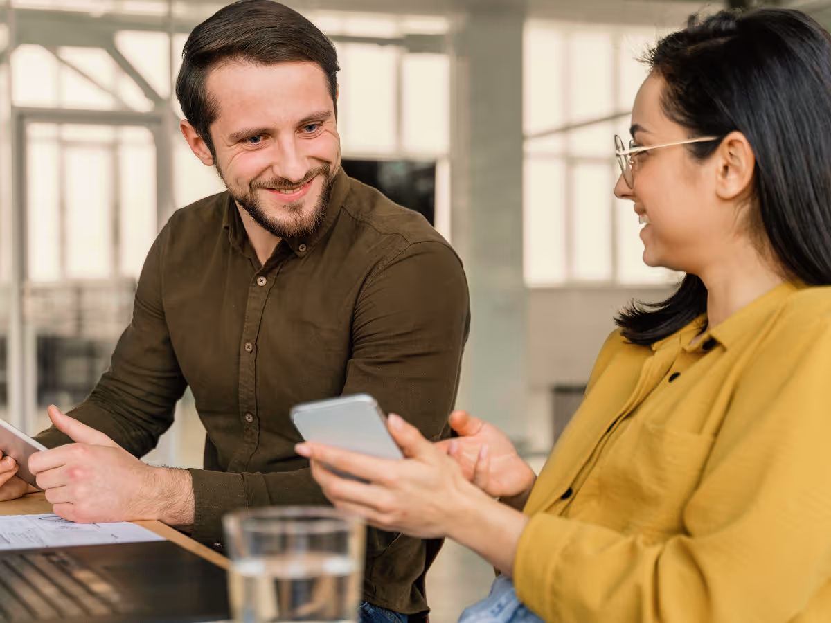 A man and a woman sitting at a table looking at a cell phone.