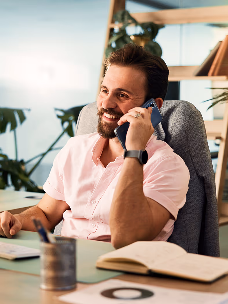 A man sitting at a desk talking on a cell phone.