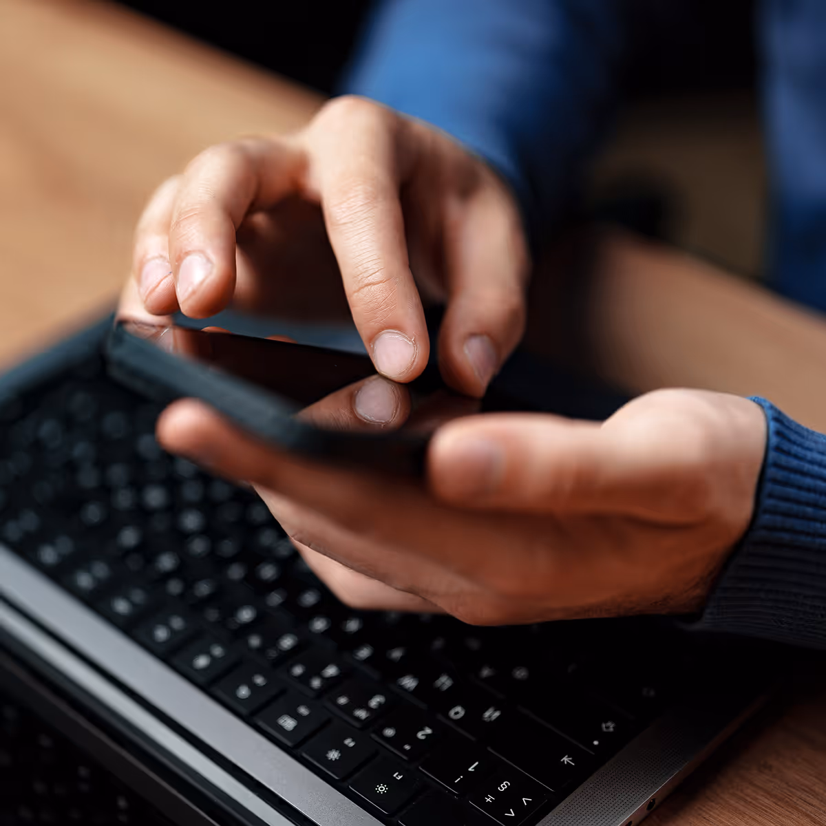A person using a cell phone on a laptop.