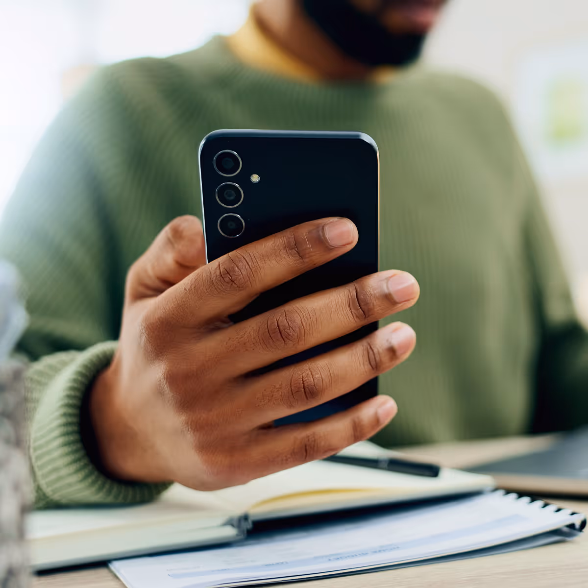 A man holding a cell phone while sitting at a desk.