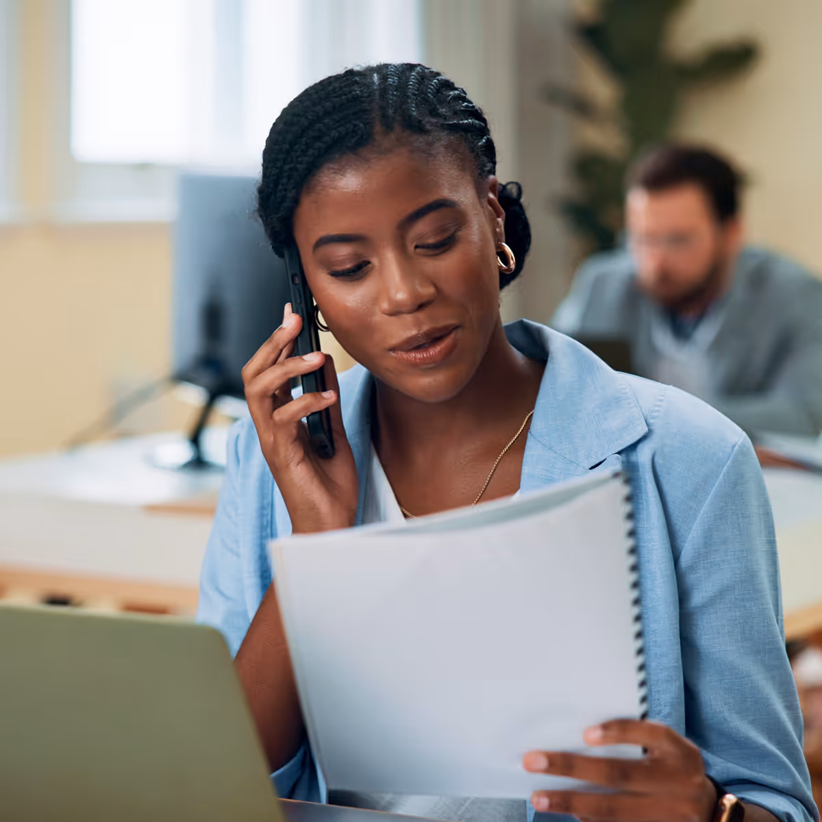 A woman sitting at a desk talking on a cell phone.