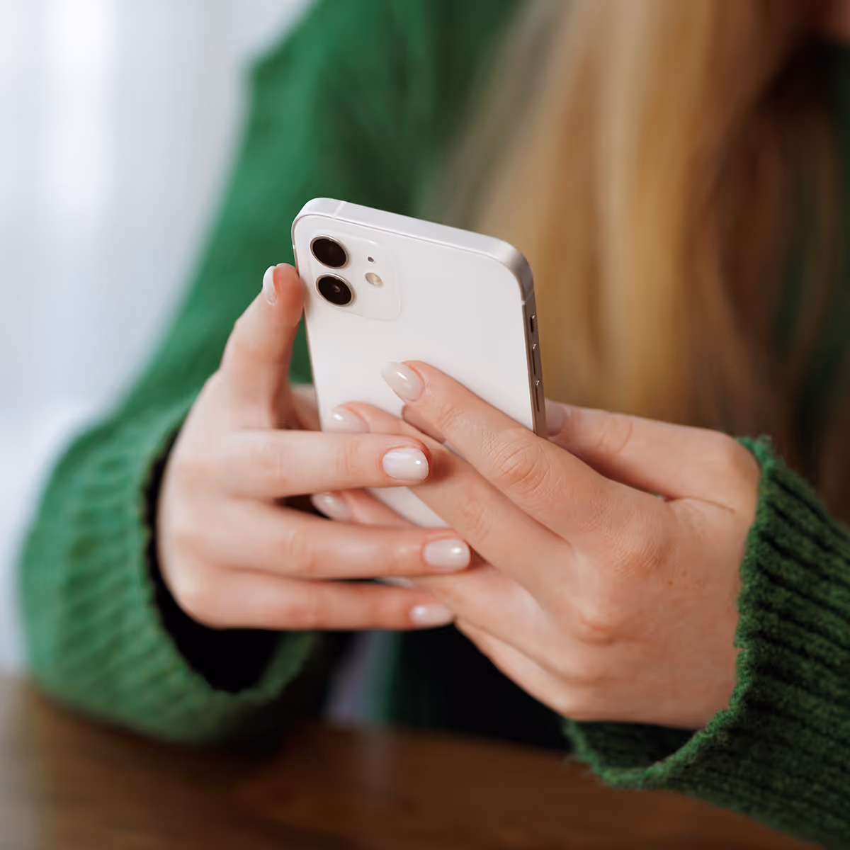 A woman in a green sweater holding a white cell phone.