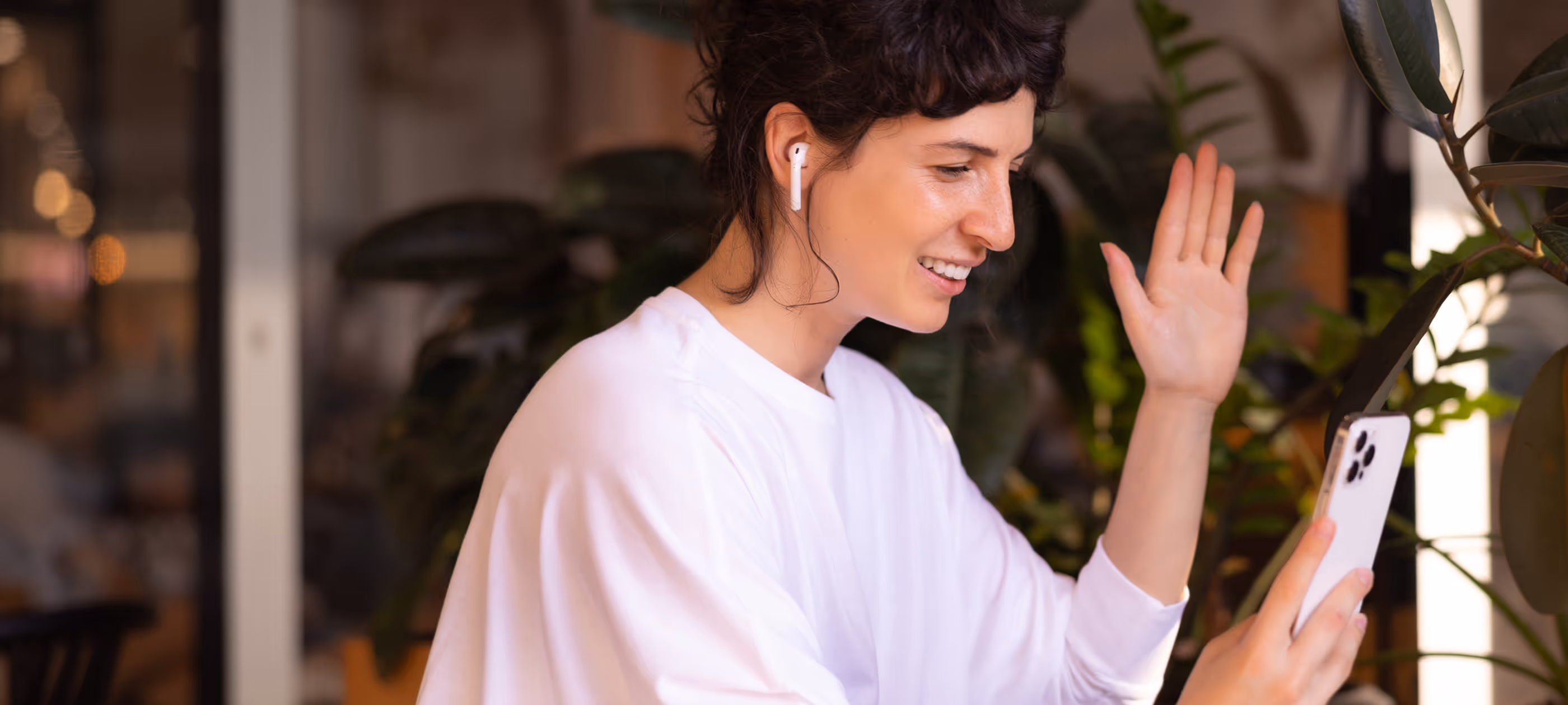 A woman standing next to a potted plant waving.