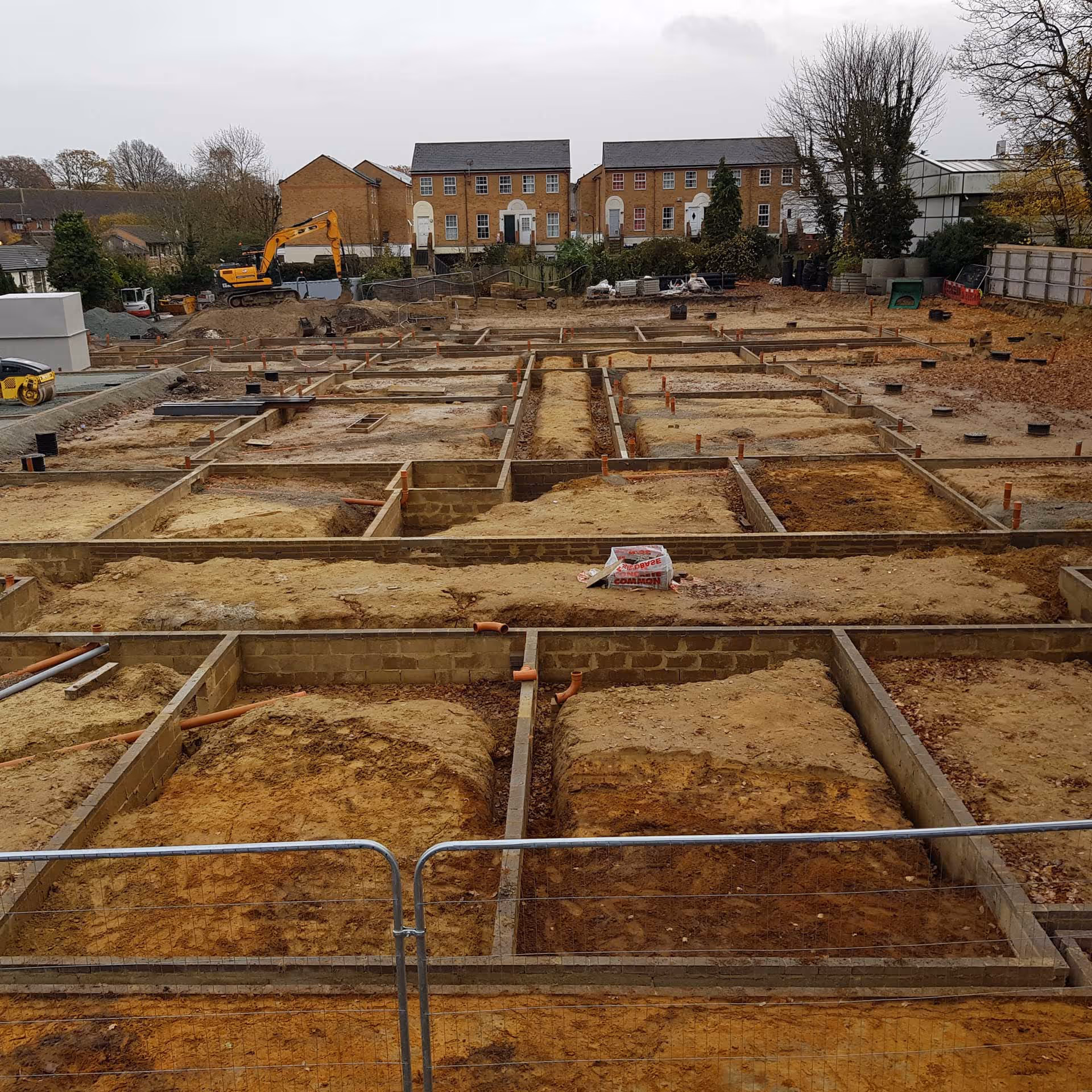 A construction site with prepared ground sections for building foundations. A digger is in the background.