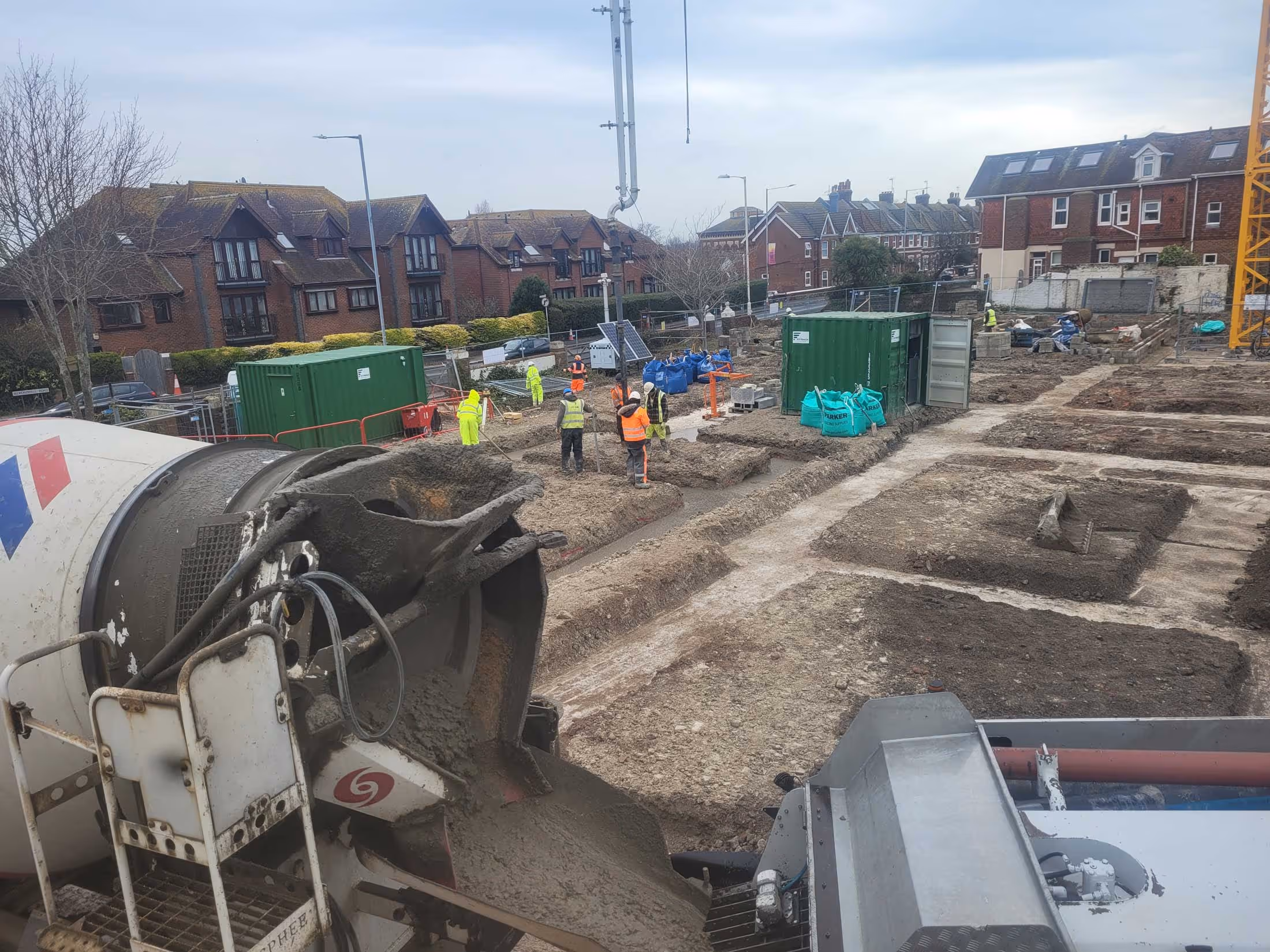 Construction workers pouring concrete from a large mixer at a building site.