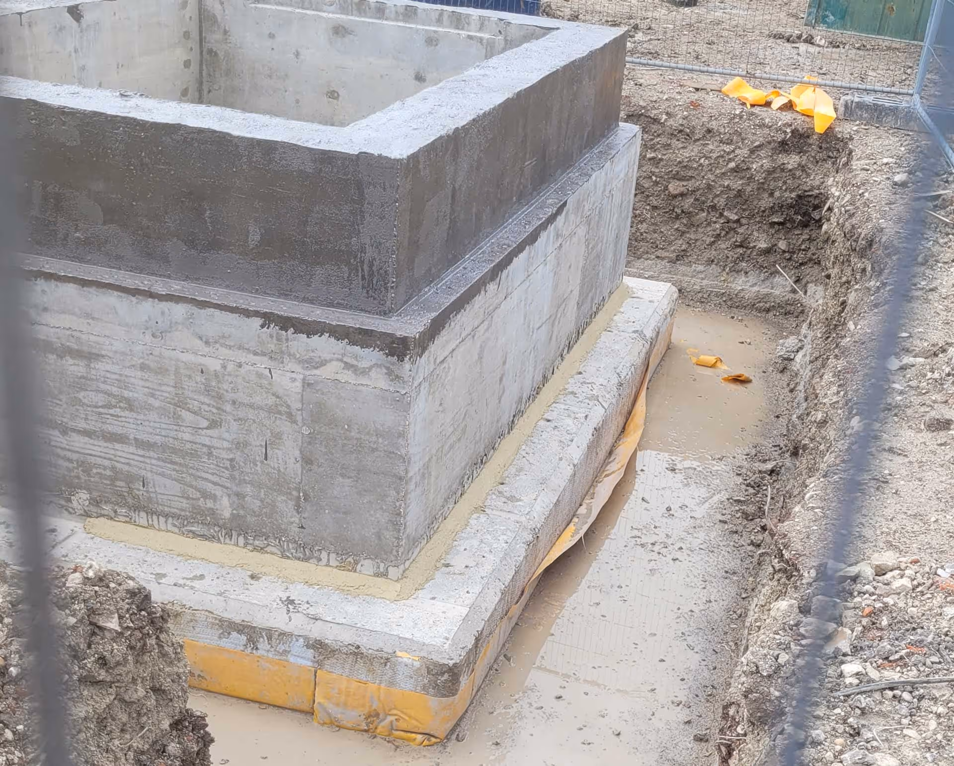 Concrete foundation structure set in a construction site trench, surrounded by muddy ground.