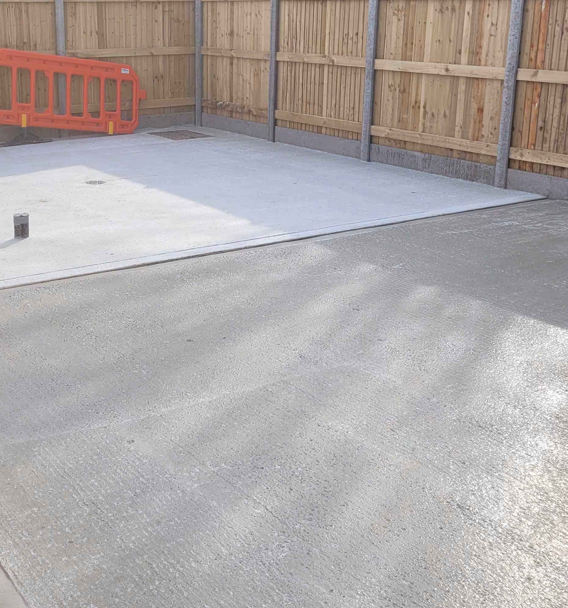 Freshly poured concrete in a small fenced area, with a bright orange barrier in the background.