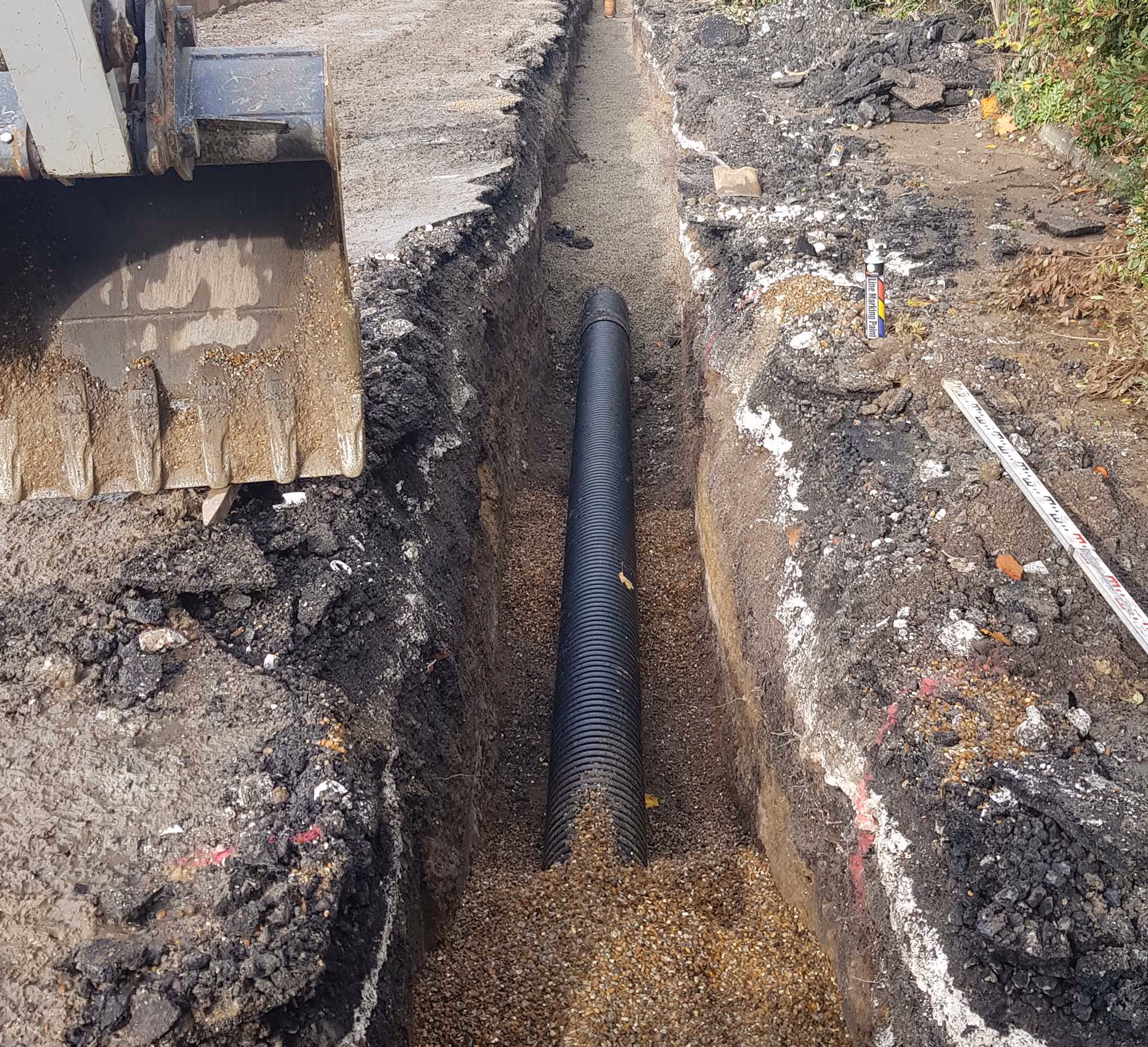 A trench next to a road contains a newly installed black drainage pipe.