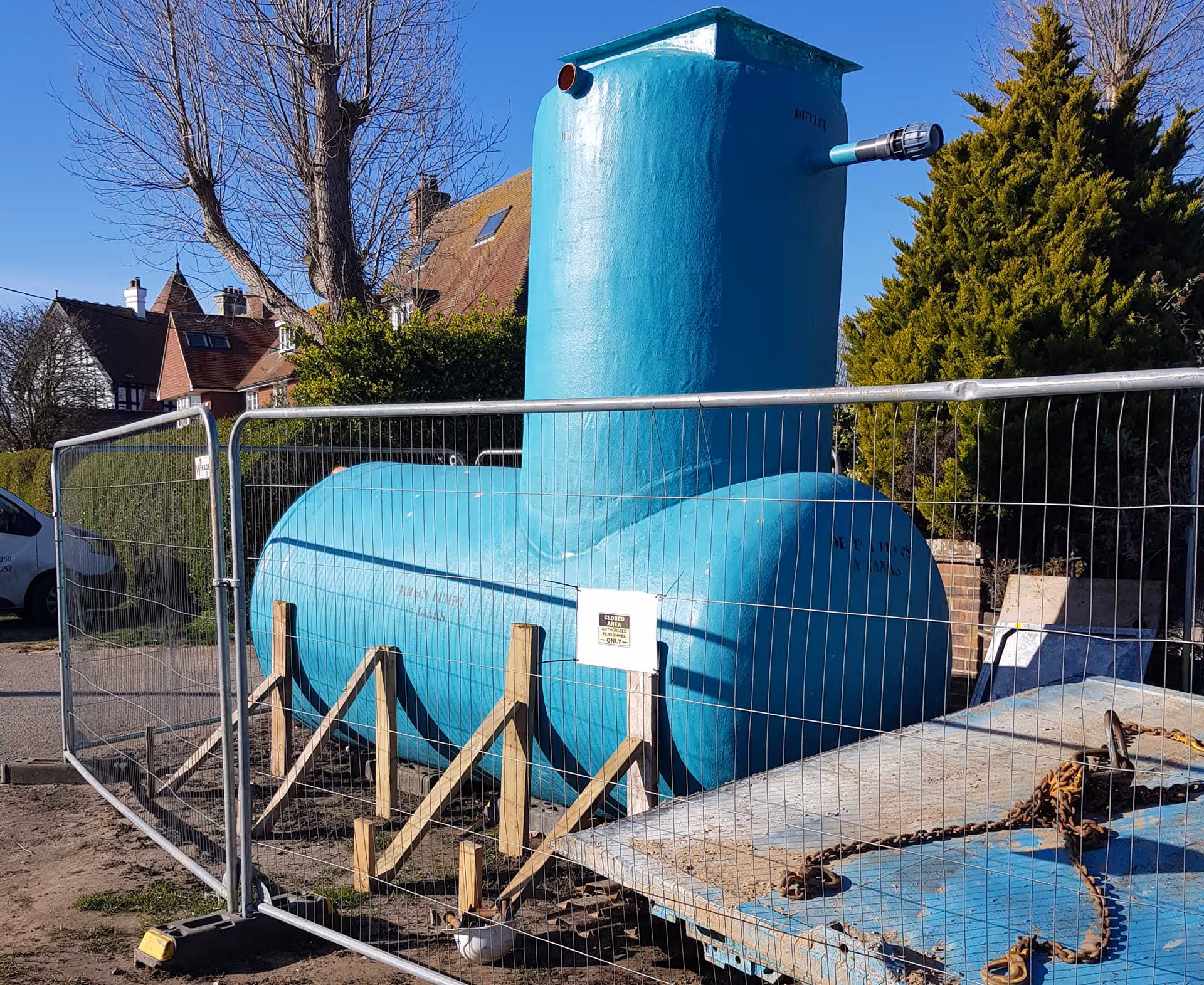 Large blue storage tank behind a metal fence, situated outdoors on a sunny day.