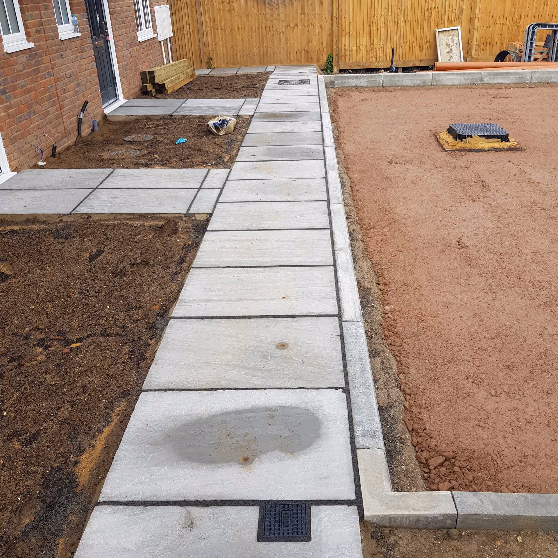 A partially completed garden path with square paving stones lies next to an unfinished dirt area.
