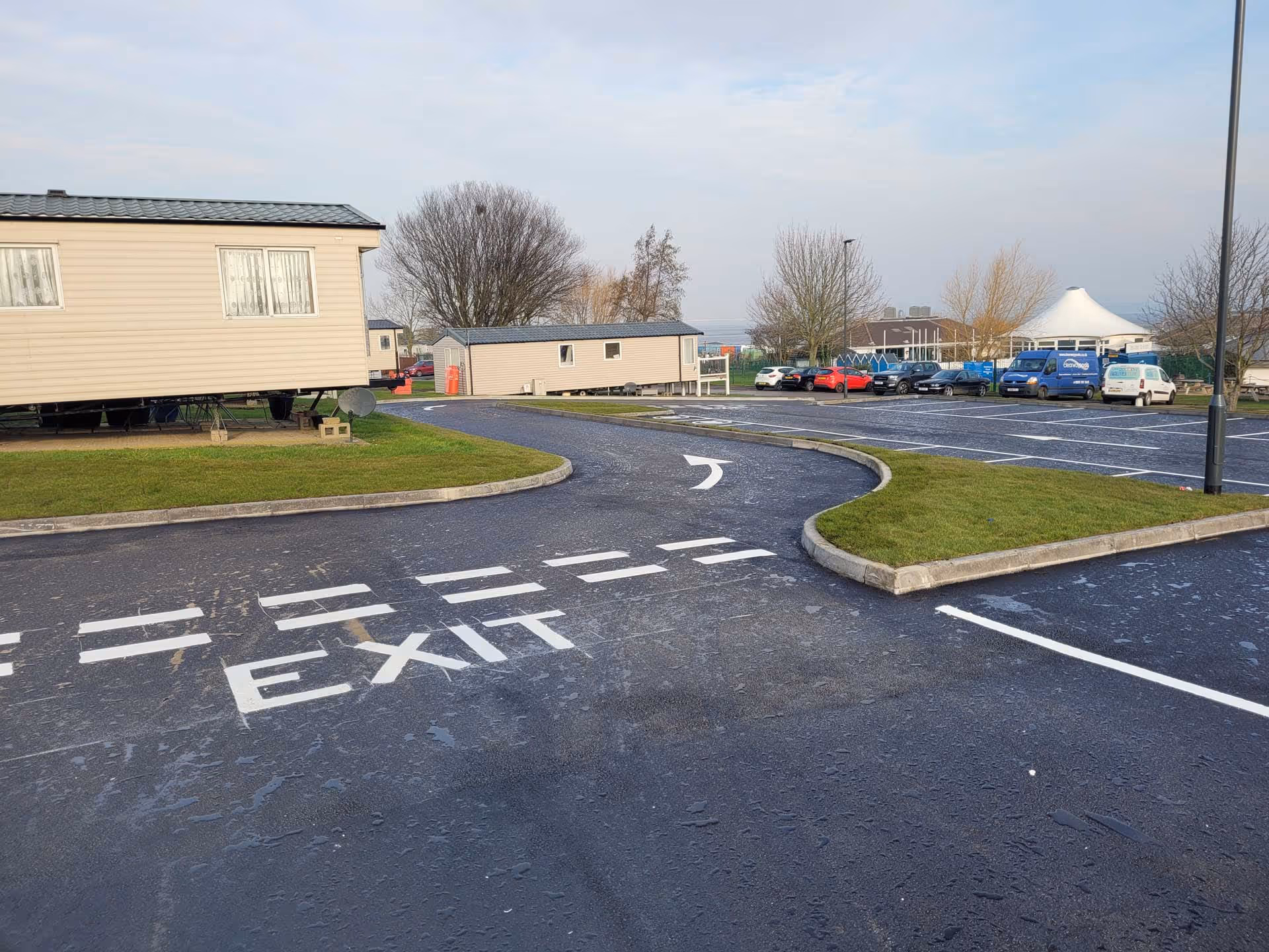 A parking lot with marked exit lanes, nearby mobile homes, and cars parked in the distance.