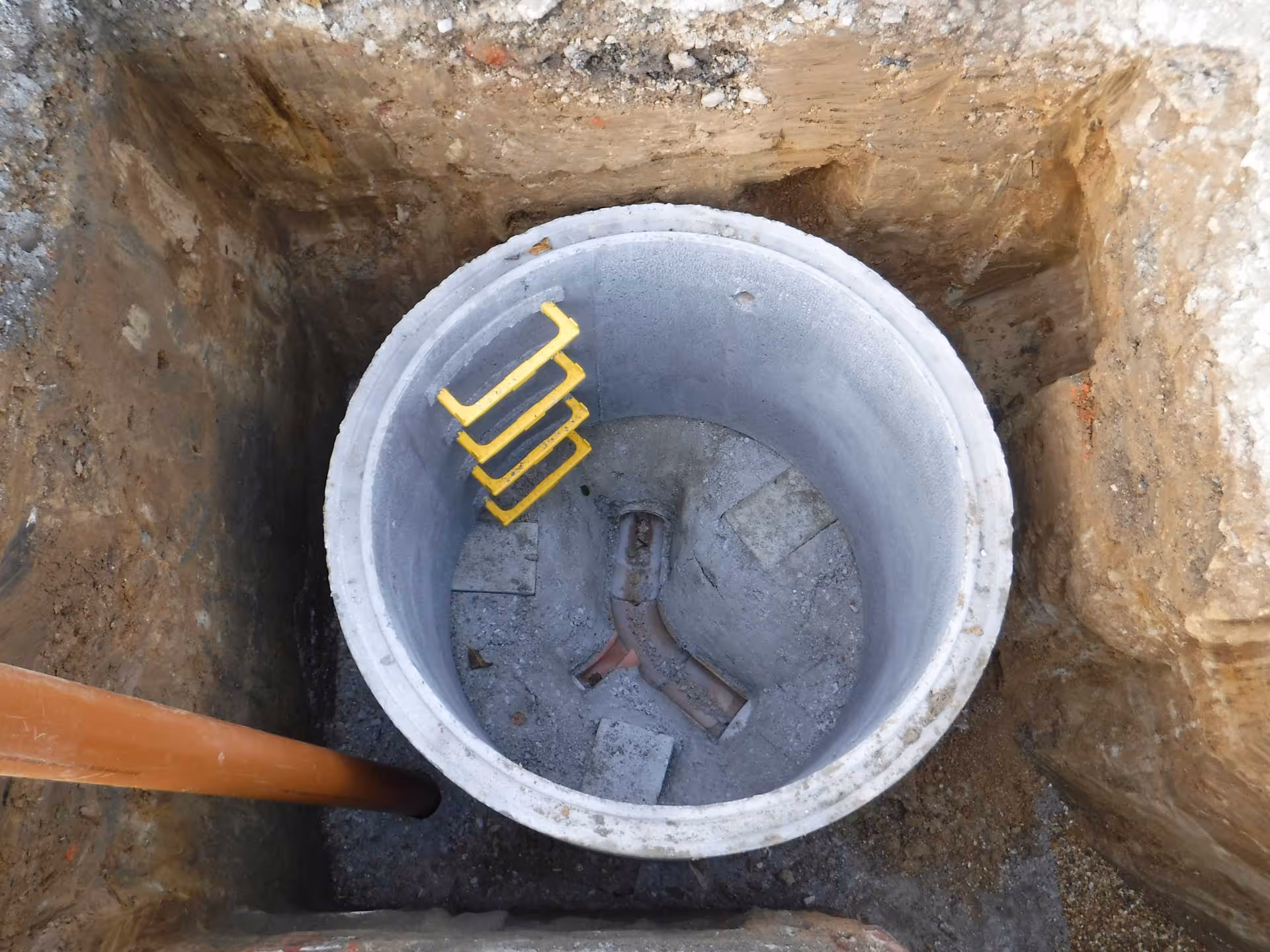 A concrete manhole with yellow metal rungs inside and a pipe entering from the left.