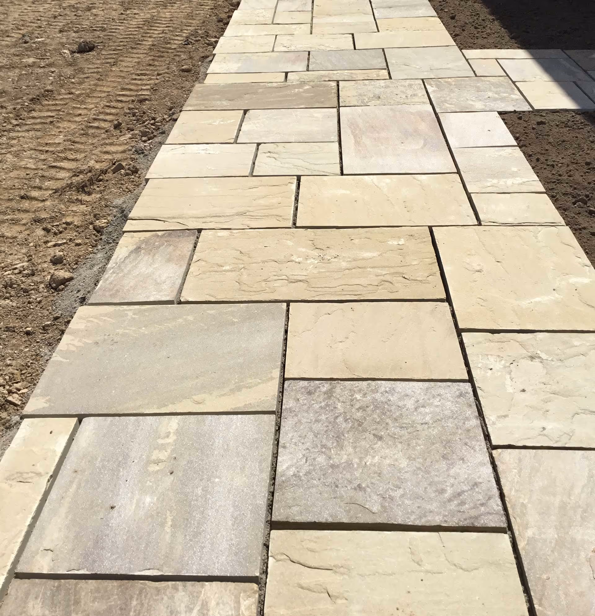 A freshly laid stone pathway with rectangular and square tiles in various shades of beige.