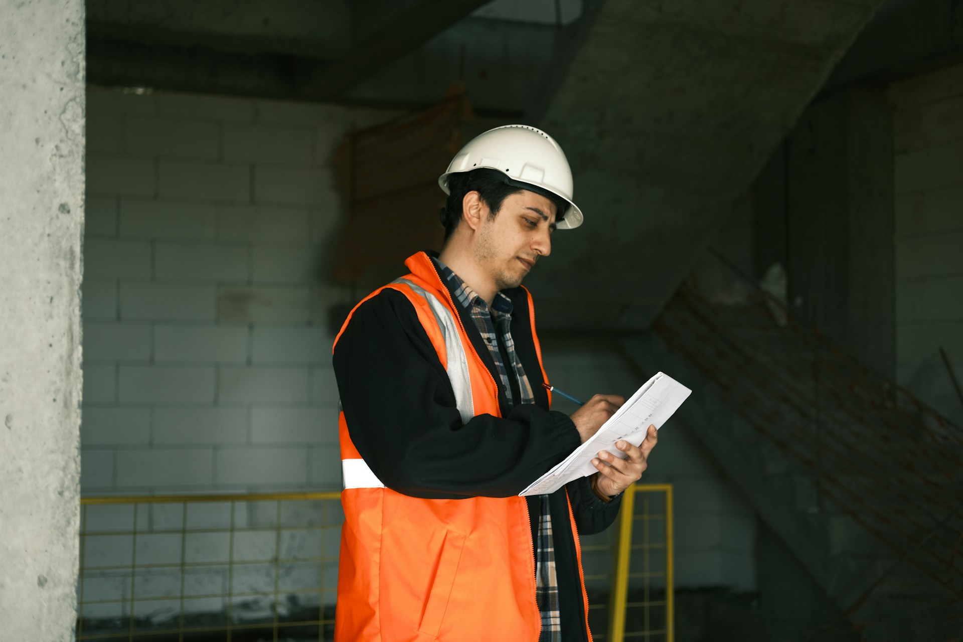 Un ouvrier vêtu d'un gilet orange et d'un casque écrit sur un plan dans un chantier