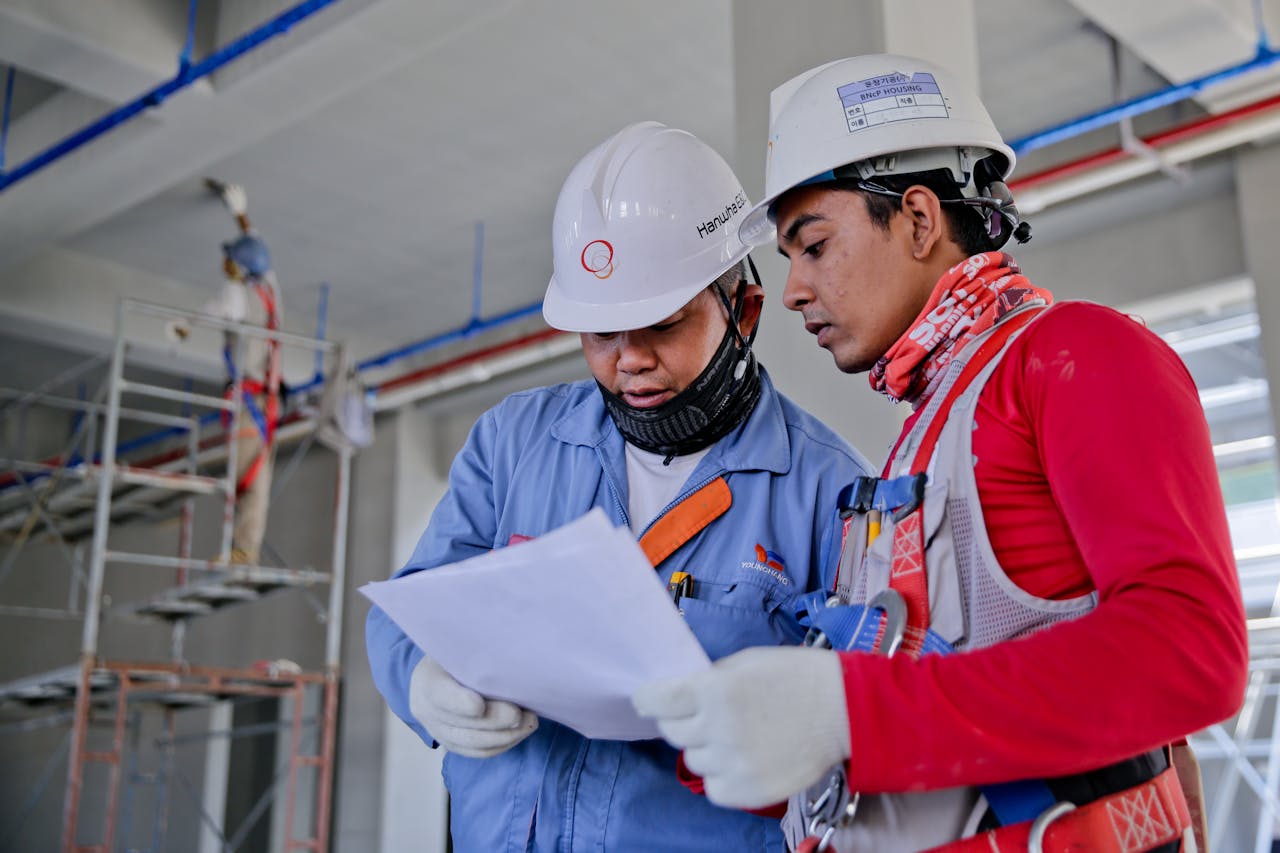 Deux installateurs électricien regardent un plan, ils portent tous les deux des combinaisons de travail et un casque