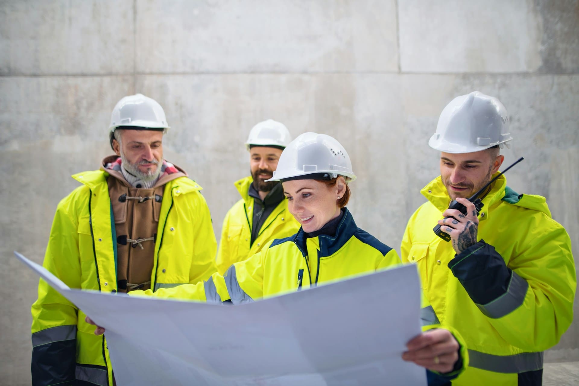 Quatre personnes portant un gilet jaune et un casque blanc observent un plan tenu par la femme au premier plan