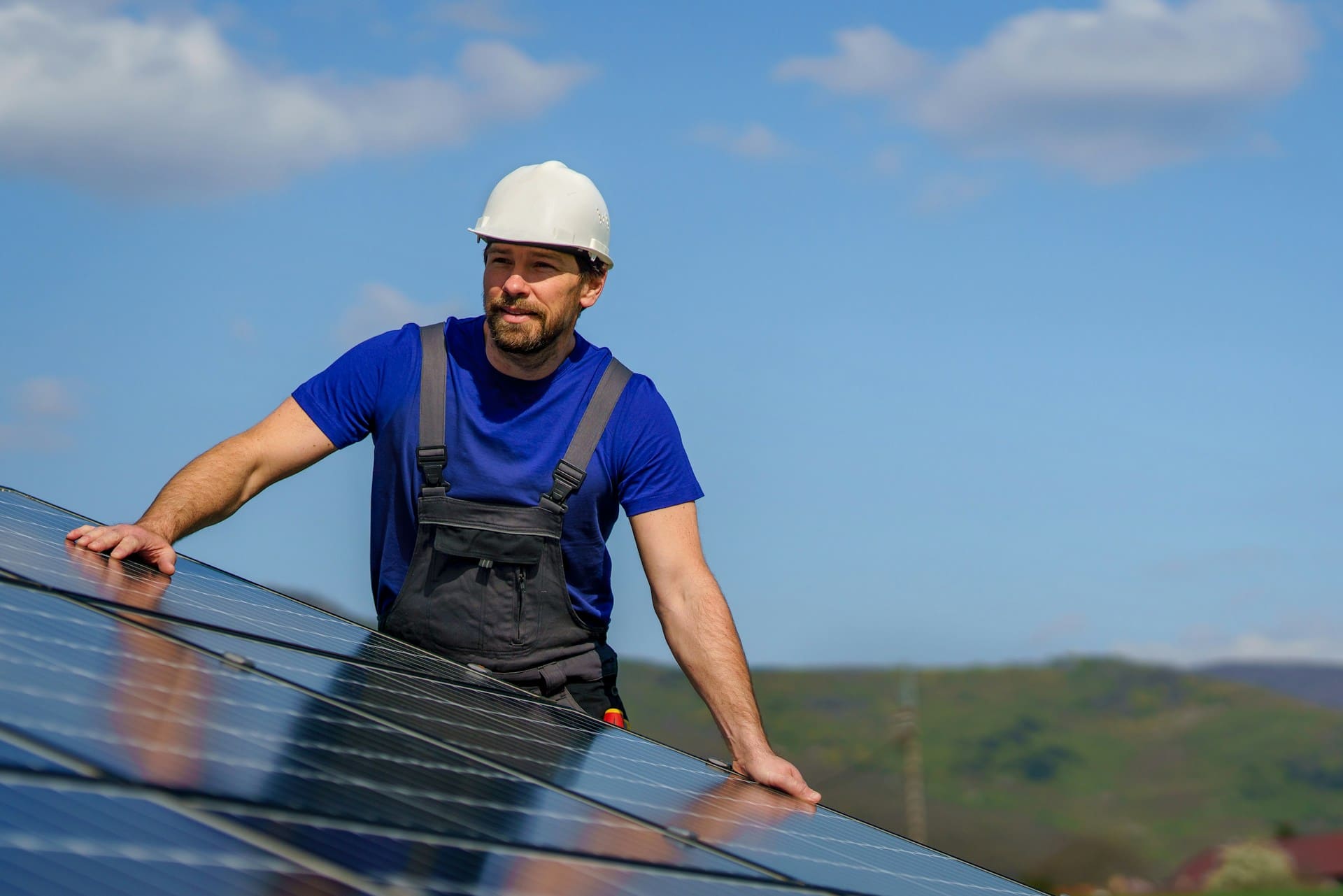 Un homme vêtu d'une salopette et portant un casque tient un panneau photovoltaïque