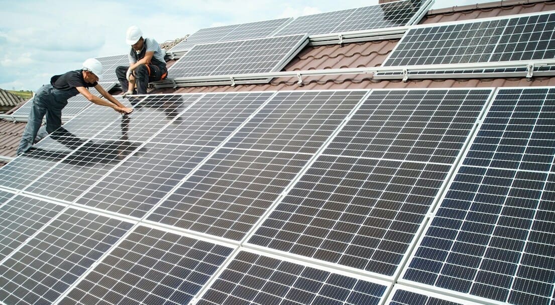 Deux installateurs de panneaux solaires travaillent sur des panneaux solaires sur un toit