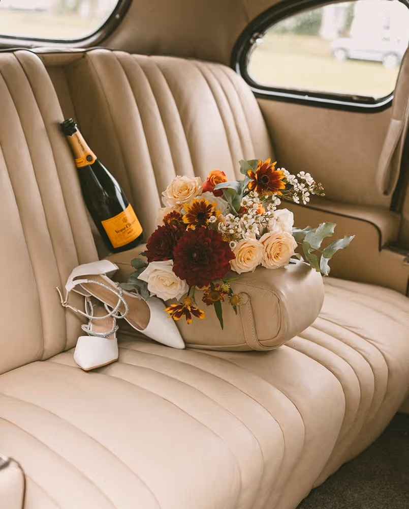 Champagne, flowers and wedding shoes in the back seat of a car.