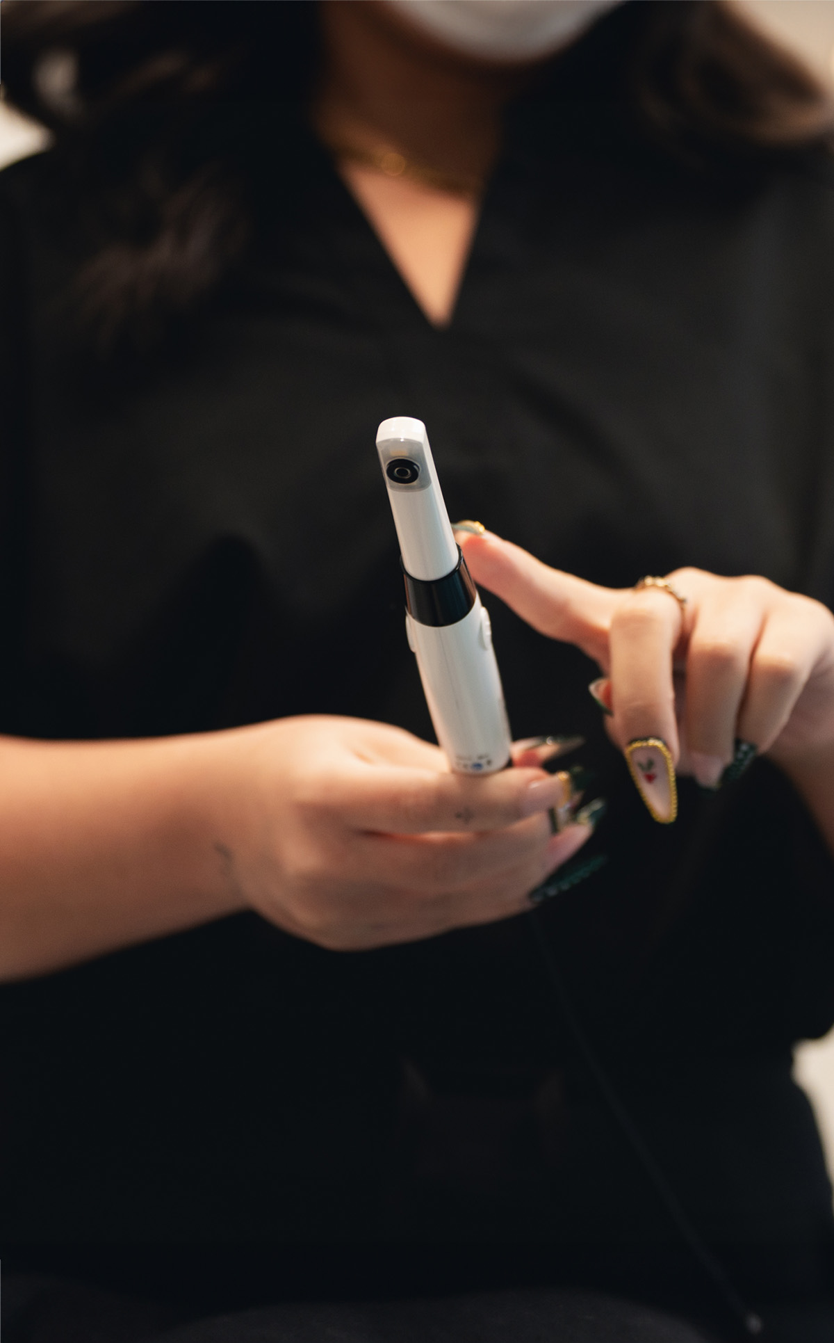 Person holding a white handheld dental or medical device with decorated nails and pointing at it.