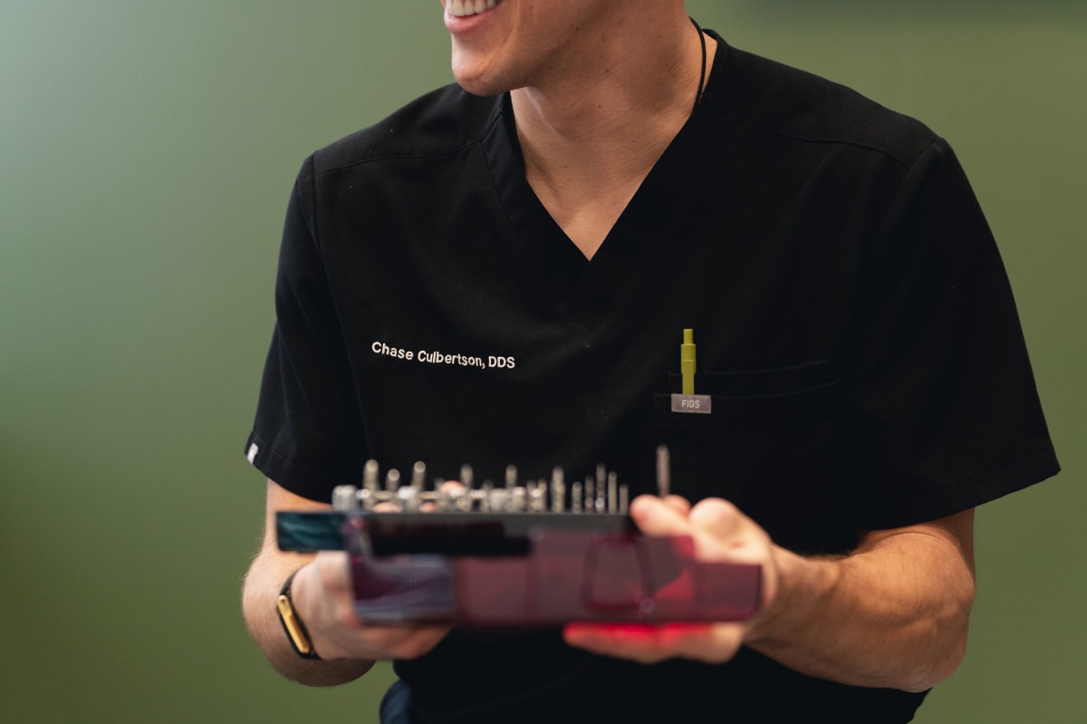 Dentist holding dental implant model showing screw structure against green background
