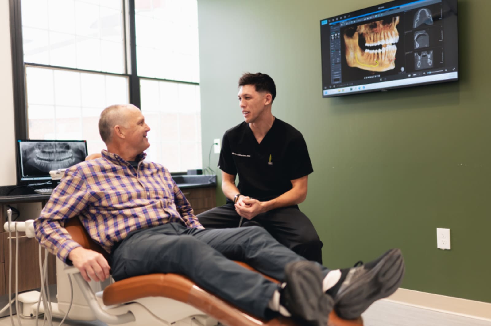Dentist consulting with patient in treatment room, pointing to digital display