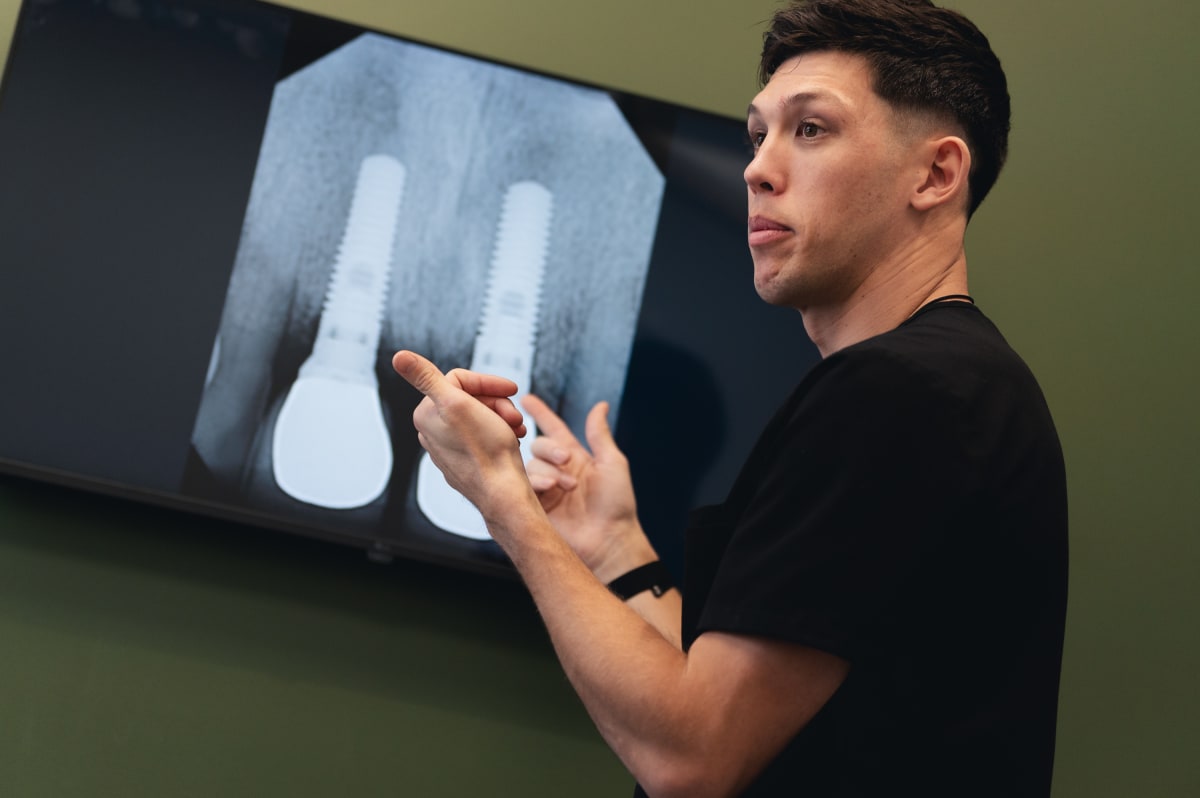 Dentist holding and explaining a dental implant model to a patient during consultation
