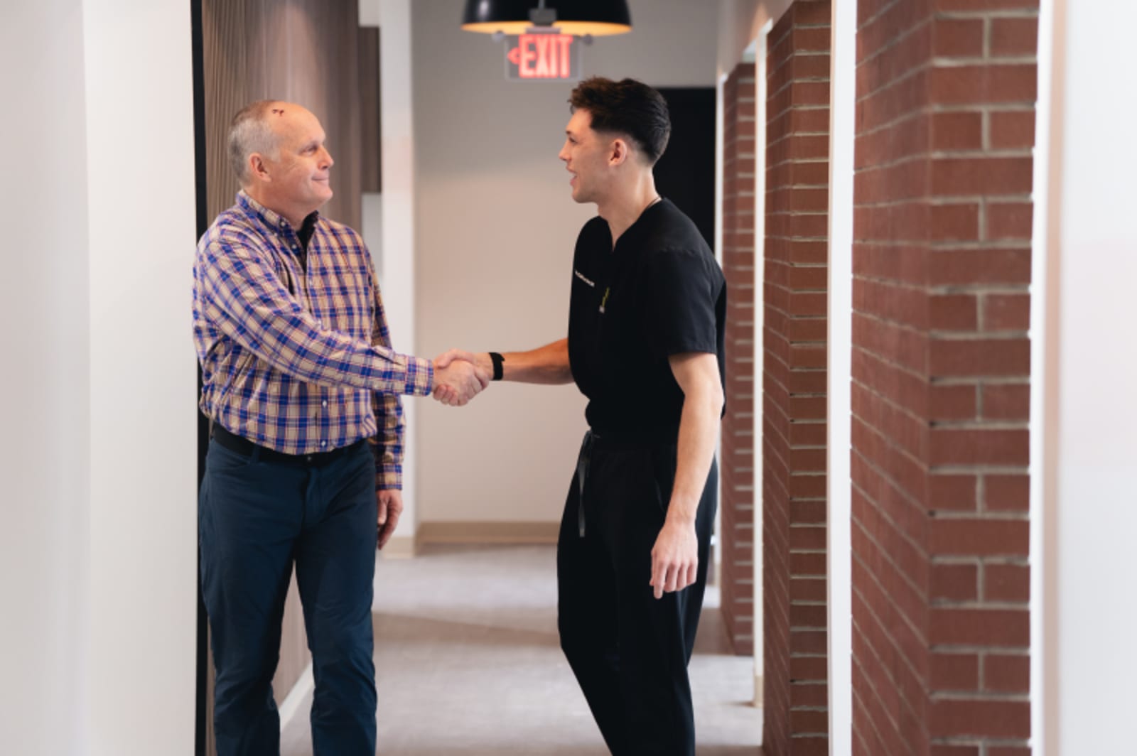 Dentist greeting and shaking hands with male patient in modern dental office hallway