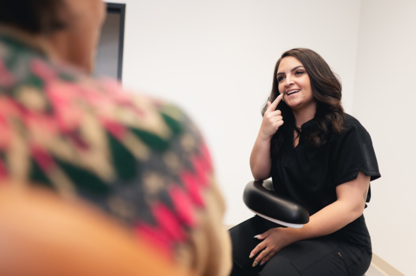 Female dental professional in dark scrubs sitting in clinical setting