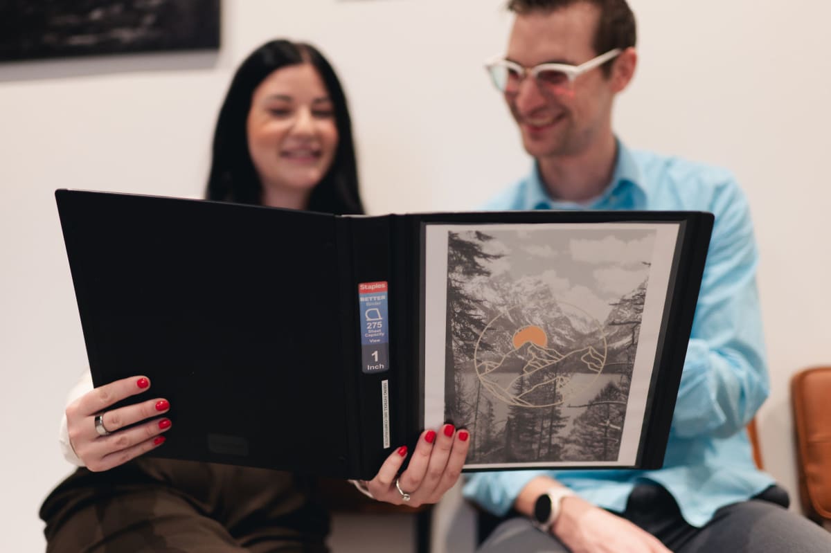 Two team members smile while reviewing a portfolio binder of photos together at the office.