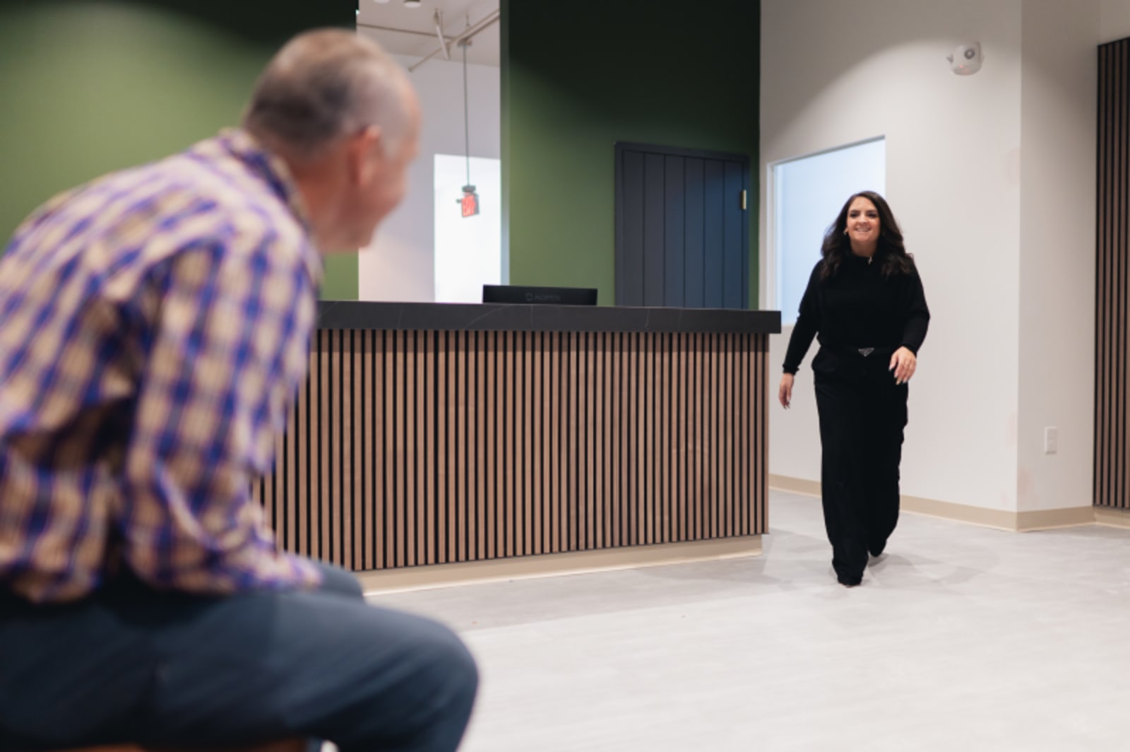 A team member walks through the practice's modern reception area toward a patient waiting near the wood-paneled front desk.