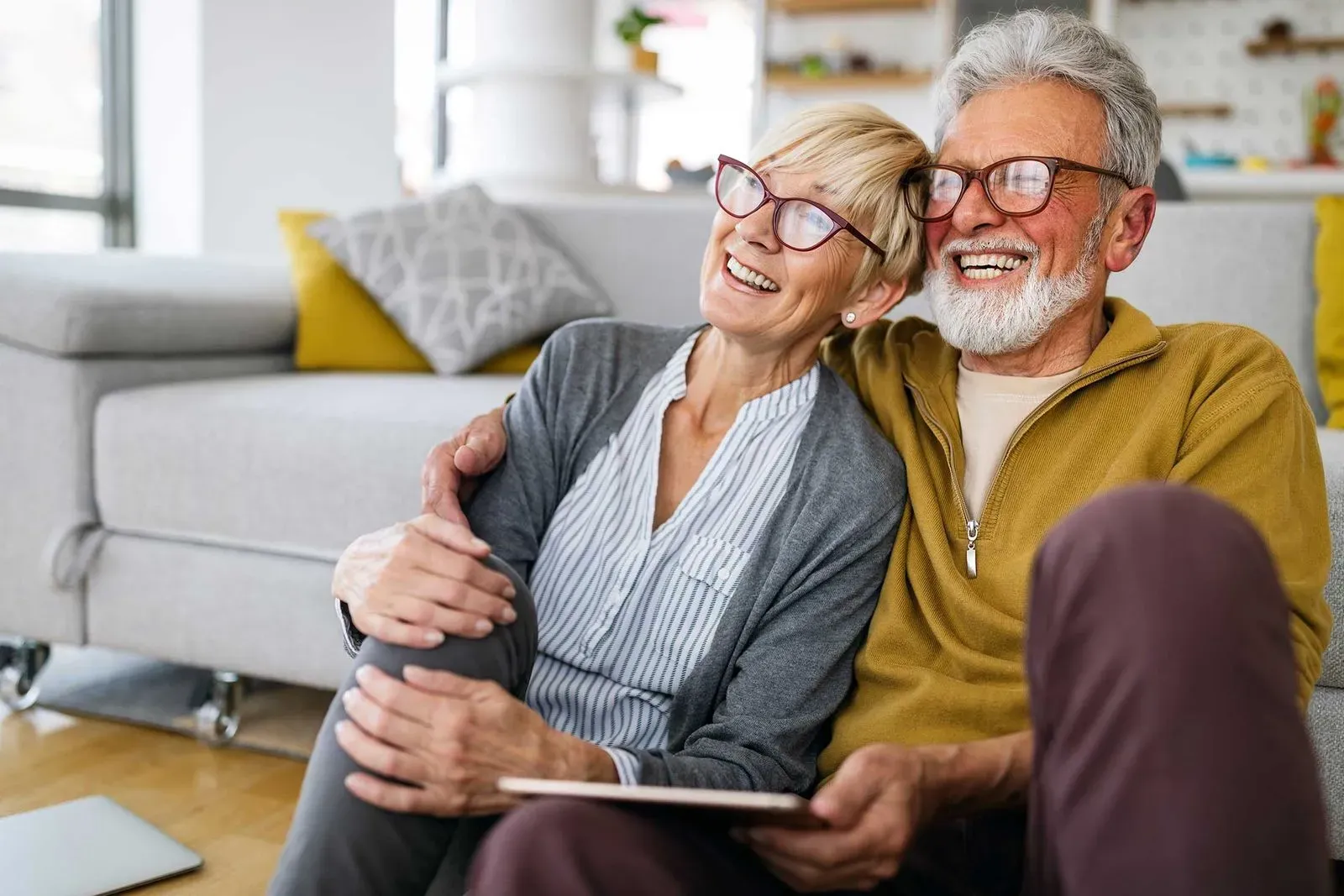 Older couple laughing together, embracing on couch at home